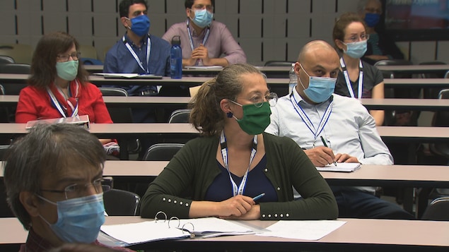 Des gens portant des masques écoutent dans une salle de classe.