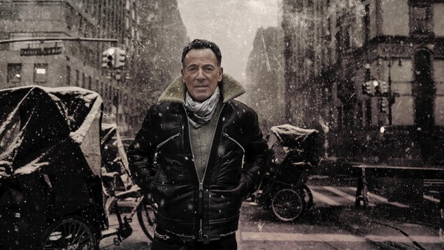 Bruce Springsteen, avec un manteau de cuir, pose dans une rue.