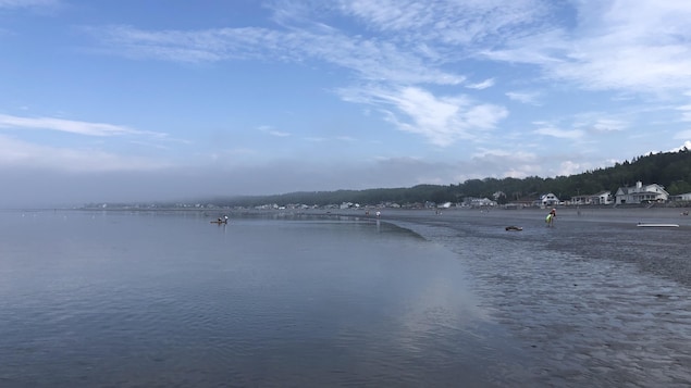 Une plage avec quelques baigneurs avec de la brume au loin.