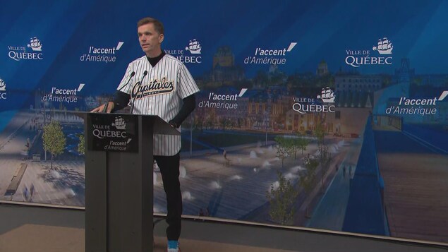 Le maire Marchand porte un chandail de baseball lors d'un point de presse. 