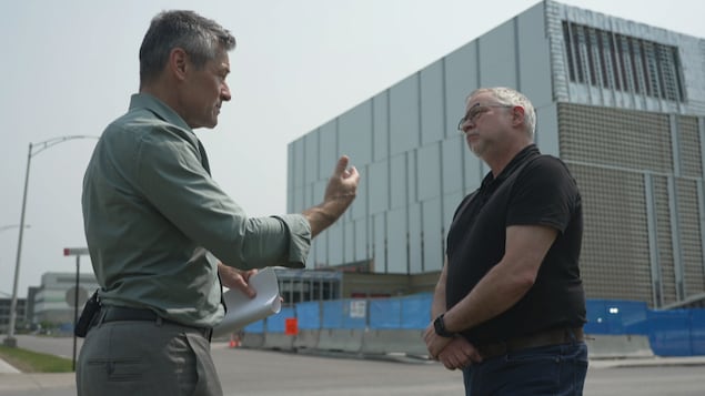 Deux hommes discutent devant un chantier de construction.