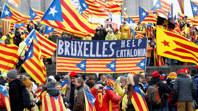 Des manifestants pro-Catalogne portent le drapeau catalan, rayé rouge et jaune, en cape. Plusieurs autres drapeaux de la Catalogne flottent au vent. Des manifestants pro-Catalogne portent le drapeau catalan, rayé rouge et jaune, en cape. Plusieurs autres drapeaux de la Catalogne flottent au vent.