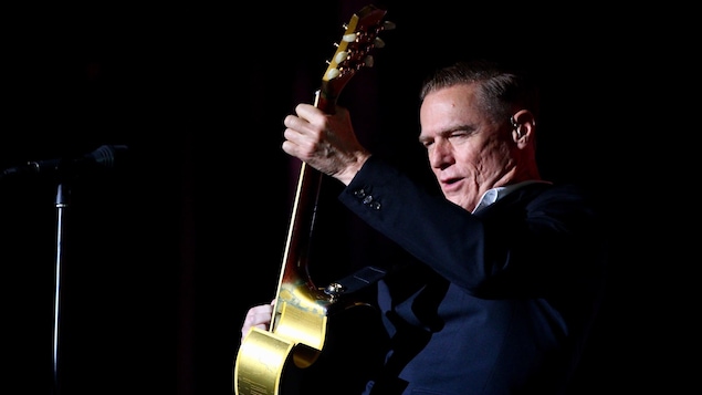 Bryan Adams sur scène avec une guitare et un micro.