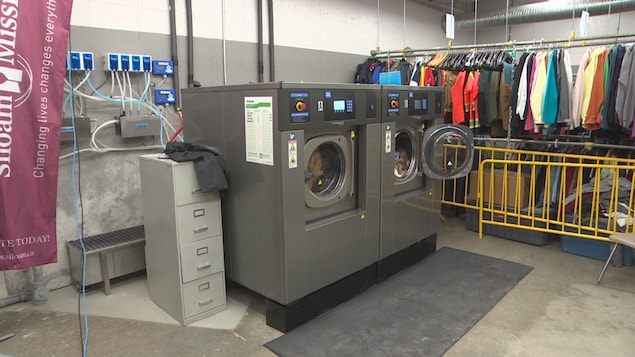 Deux laveuses commerciales à côté desquelles des vêtements sont suspendus à des cintres.
