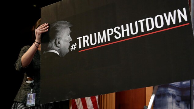 On peut lire sur la pancarte noire le mot-clic #TrumpShutDown