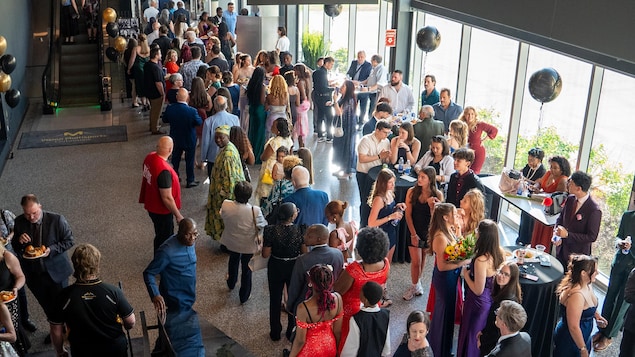 Plusieurs personnes en tenue de bal mangent et discutent autours de tables hautes.