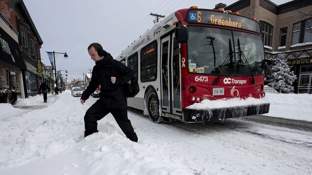 Un hombre camina por un banco de nieve junto a un autobús de la ciudad de Ottawa.