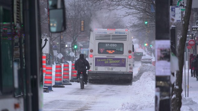 Un cycliste suit de près un autobus sur une chaussée enneigée.