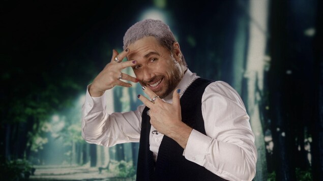 Stéphane Rousseau porte du vernis sur ses ongles et a le dessus des cheveux teint en blanc.