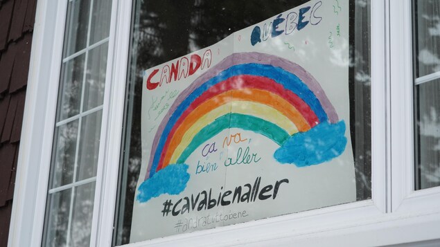 Une dessin d'arc-en-ciel avec le slogan «Ça va bien aller» affichés dans la fenêtre d'une maison