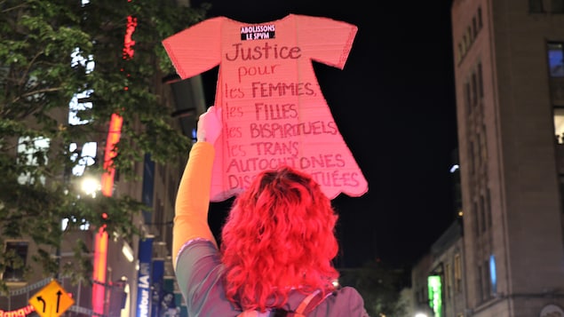 Une femme de dos tient une pancarte.