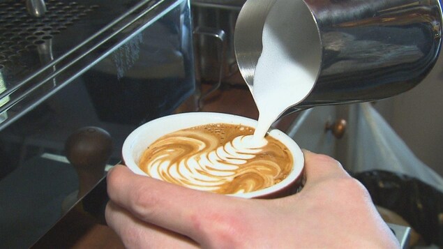Un barista dessine avec de la mousse de lait sur un latte. 