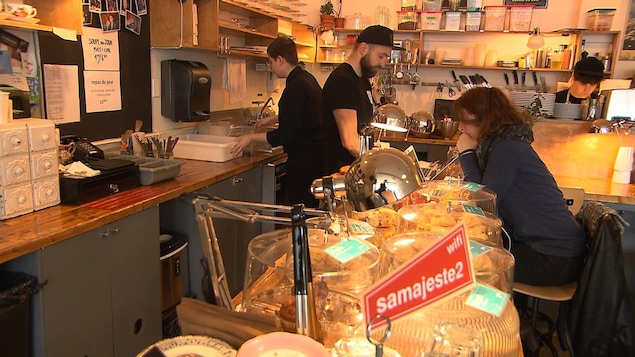 Les employés d'un café travaillent derrière un comptoir, où se trouve une cliente.