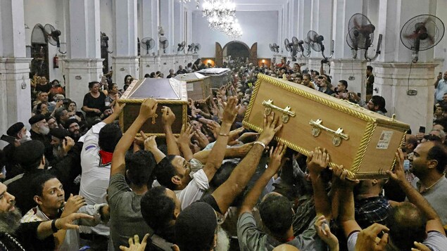 Des centaines de personnes entassées dans une église transportent des cercueils. 