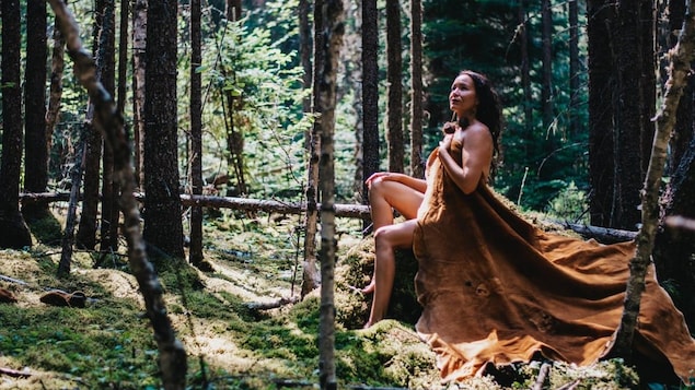 امرأة تجلس على صخرة في الغابة، وجسدها العاري مغطى بقطعة جلد كبيرة.