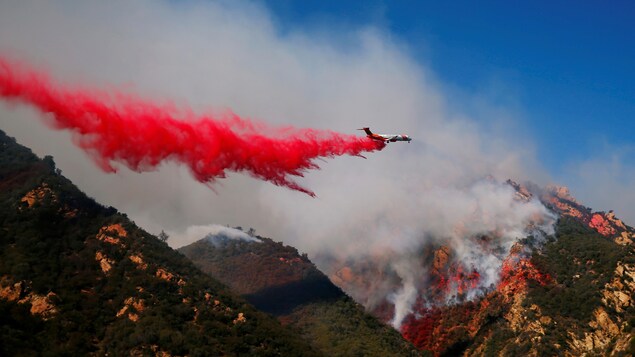 Un avion lâche un genre de poudre rouge au-dessus de montagnes envahies de fumée. Un avion lâche un genre de poudre rouge au-dessus de montagnes envahies de fumée.
