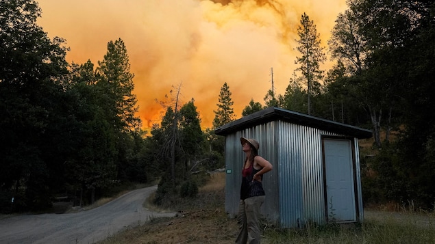 Une femme se tient à l'extérieur de sa cabane, alors qu'un feu agricole vient enfumer le paysage.