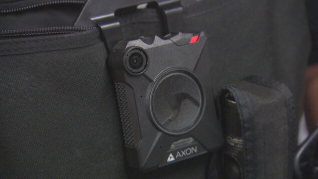 Zoom sur la caméra, plus petite qu'un téléphone cellulaire, sur le gilet d'un policier.