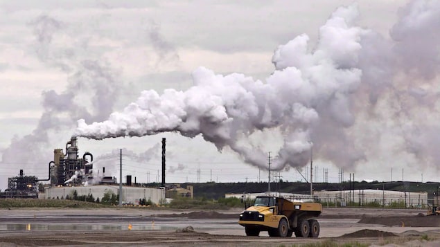 شاحنة صفراء ضخمة وانبعاثات ثاني أكسيد الكربون من منشأة لاستخراج النفط من الرمال الزفتية.