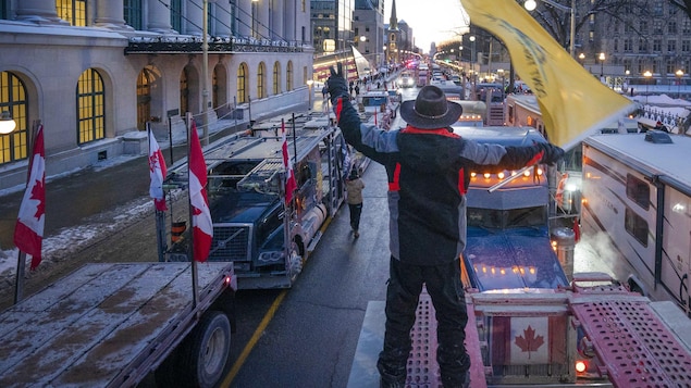 Un homme agite un drapeau depuis le toit d'un camion sur la rue Wellington à Ottawa.