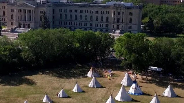 Vue aérienne d'un camp de tipis dans un parc, devant un grand bâtiment de style néo classique. Vue aérienne d'un camp de tipis dans un parc, devant un grand bâtiment de style néo classique.