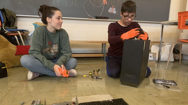 Un garçon manipule des pièces pour construire un appareil électronique et une jeune fille à côté de lui le regarde.