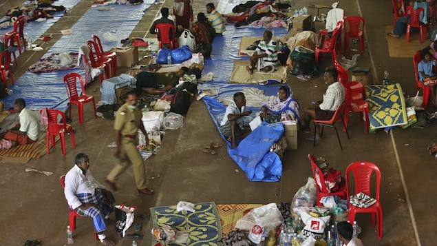 Des sinistrés sont installés dans un campement à Cochin, dans le Kerala. Ils sont assis sur des chaises ou couchés sur des couvertures posées sur le sol.