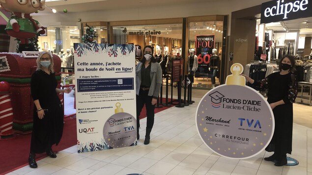 Les trois femmes posent en tenant des affiches de la campagne des boules de Noël, masquées dans le centre commercial.