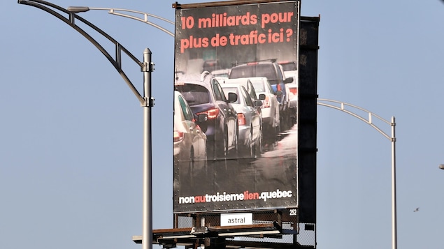 Un grand panneau publicitaire en bordure d'une autoroute de Québec sur lequel est écrite la phrase « 10 milliards pour plus de trafic ici? ».