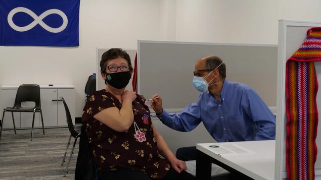 Une femme reçoit son vaccin contre la COVID-19 dans le bras, administré par un homme.
