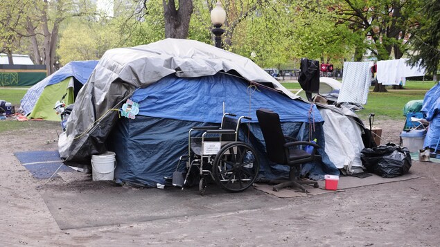 Une tente, un fauteuil roulant et d'autres objets dans un campement de sans-abri.