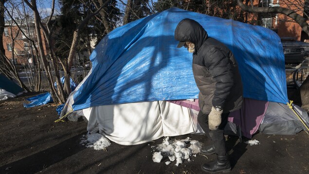 Un homme habillé chaudement debout devant sa tente.