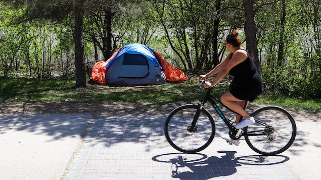 Une femme passe devant un campement en vélo.