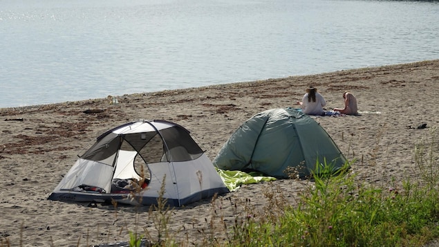 Deux tentes et deux personnes installées sur une plage.