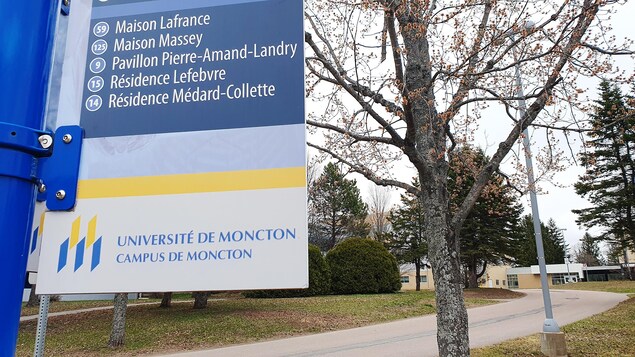 Près d'un sentier, un panneau jaune et bleu indique les directions pour se rendre aux différents pavillons et édifices de l'université.