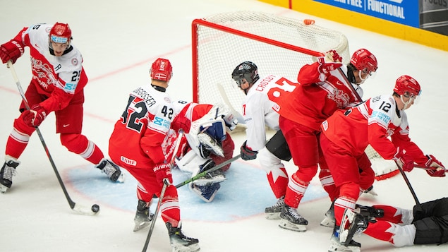 Des joueurs de deux équipes de hockey devant le filet d'un gardien. 