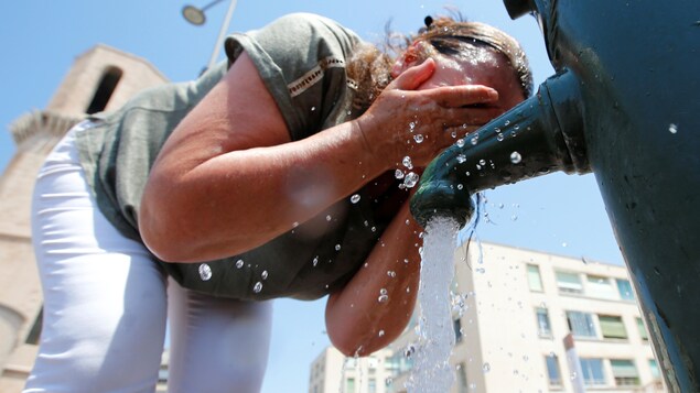 Une femme penchée devant une fontaine se mouille la figure.