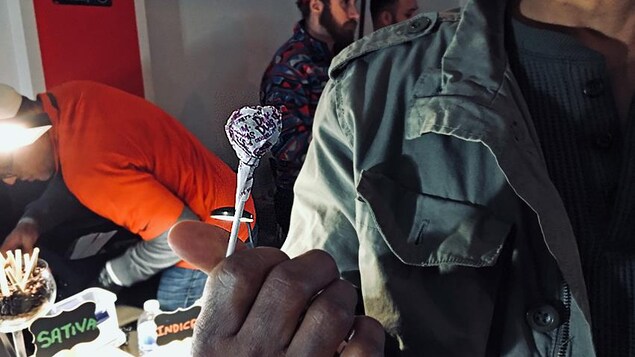 Un client d'un marché aux puces sur le thème du cannabis se trouve dans un sous-sol d'un restaurant éthiopien, toujours ouvert après les heures d'ouverture. Il présente un suçon au raisin qu'il a payé 50 $. Il a aussi reçu un « cadeau gratuit » de marijuana. Un client d'un marché aux puces sur le thème du cannabis se trouve dans un sous-sol d'un restaurant éthiopien, toujours ouvert après les heures d'ouverture. Il présente un suçon au raisin qu'il a payé 50 $. Il a aussi reçu un « cadeau gratuit » de marijuana.
