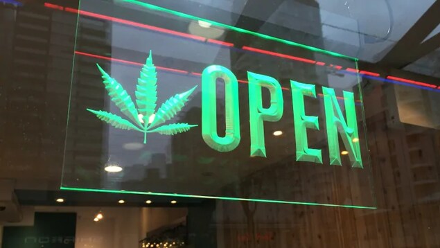 Un panneau annonçant ouvert en anglais avec une feuille de cannabis sur une vitrine de magasin.