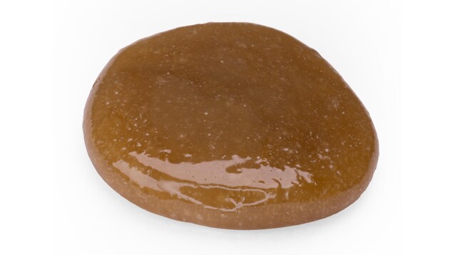 Image d'une substance visqueuse de couleur brunâtre sur fond blanc.