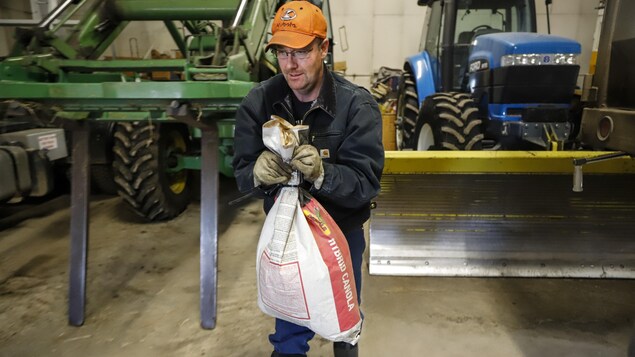 Un homme transporte un sac devant deux tracteurs stationnés dans un hangar.