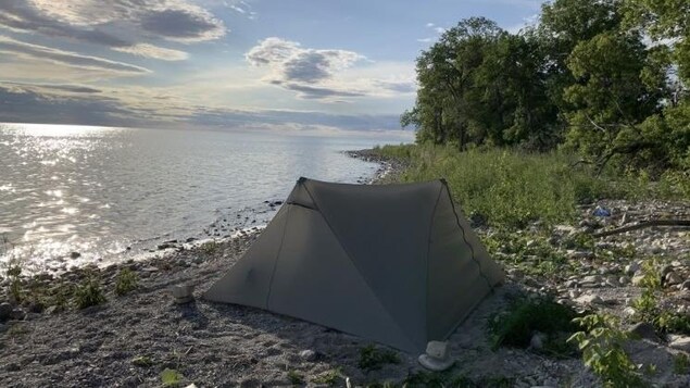 Une tente grise installée sur la plage d'un lac.