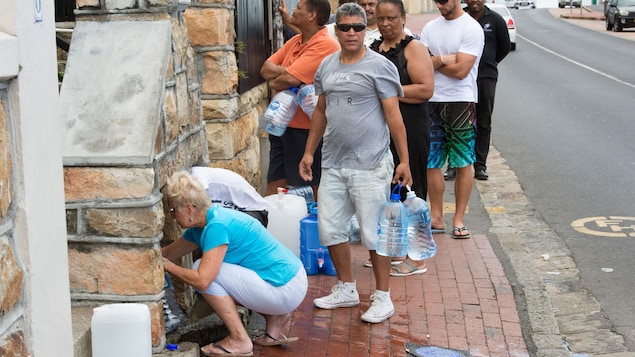 Des citoyens du Cap font la file sur le trottoir avec des bidons de plastique pour s'approvisionner en eau potable à l'aide d'un tuyau lié à une source souterraine.