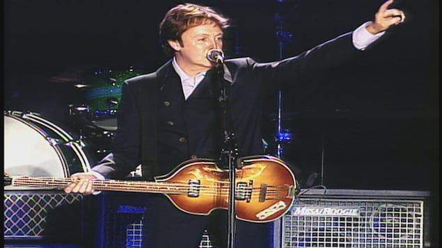 Paul McCartney s'adresse à la foule en tenant sa basse. 
