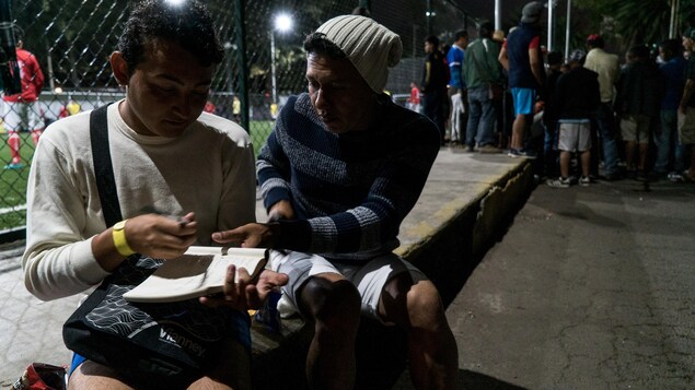 Deux hommes sont assis près d'un terrain où se joue un match de baseball. Deux hommes sont assis près d'un terrain où se joue un match de baseball.