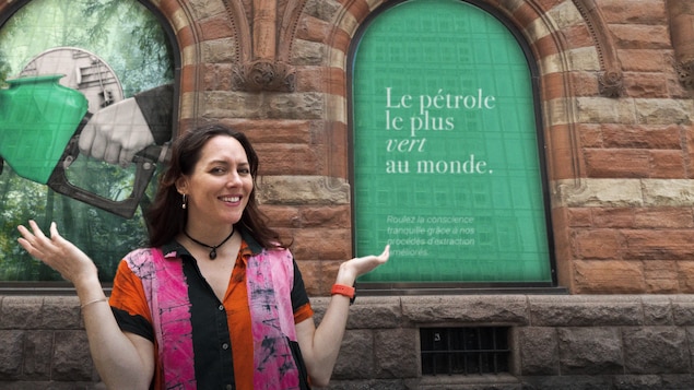 Une femme se tient devant une publicité de pétrole vert.