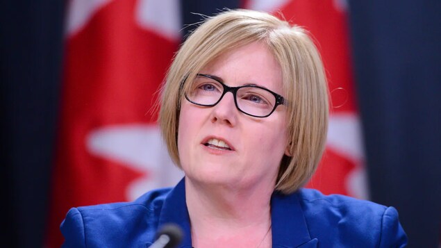Close up shot ni Carla Qualtrough at nasa likod niya ang watawat ng Canada.