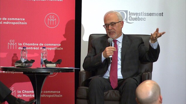 Carlos Leitao assis sur une chaise, sur la scène, parle dans un micro.