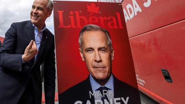 Mark Carney posa unto a un afiche de campaña.