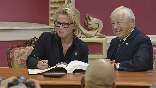 Caroline Proulx signe le registre officiel, assise à côté du lieutenant-gouverneur. Caroline Proulx signe le registre officiel, assise à côté du lieutenant-gouverneur.